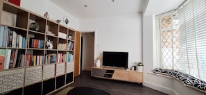 A living room with a bookshelf, a TV, and a window with blinds. - Charming London period house (London)