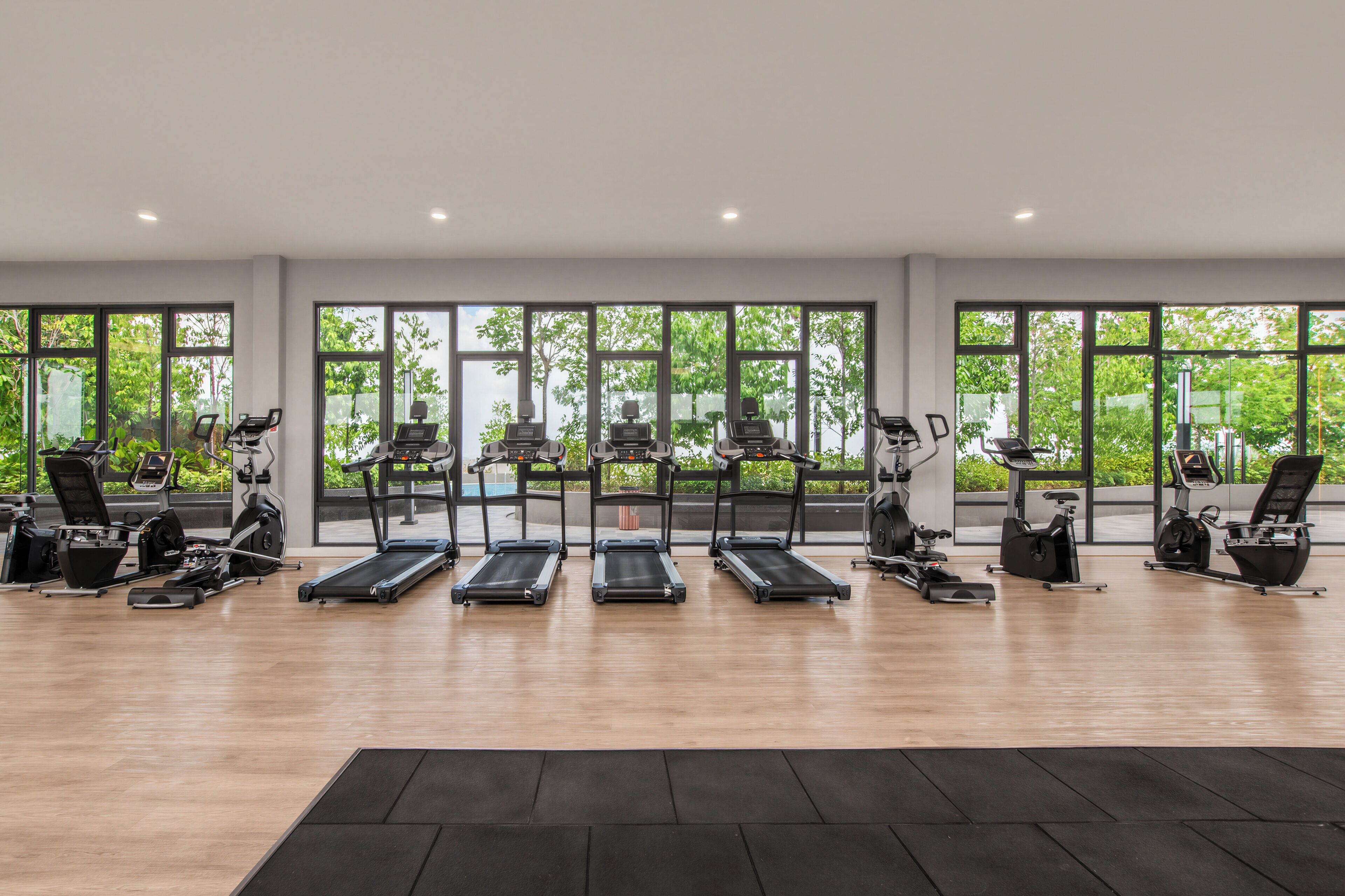 A gym with treadmills, elliptical machines, and stationary bikes arranged in rows.