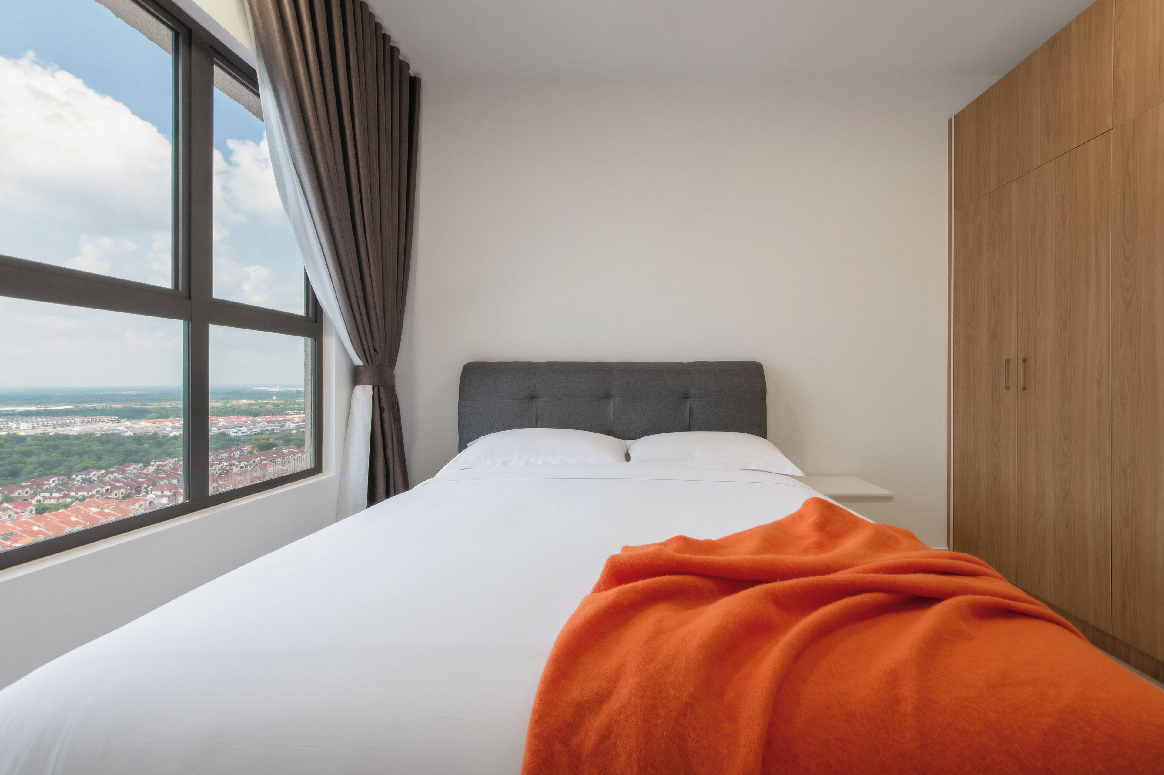 A hotel room with a bed, a window with curtains, and a view of a cityscape.