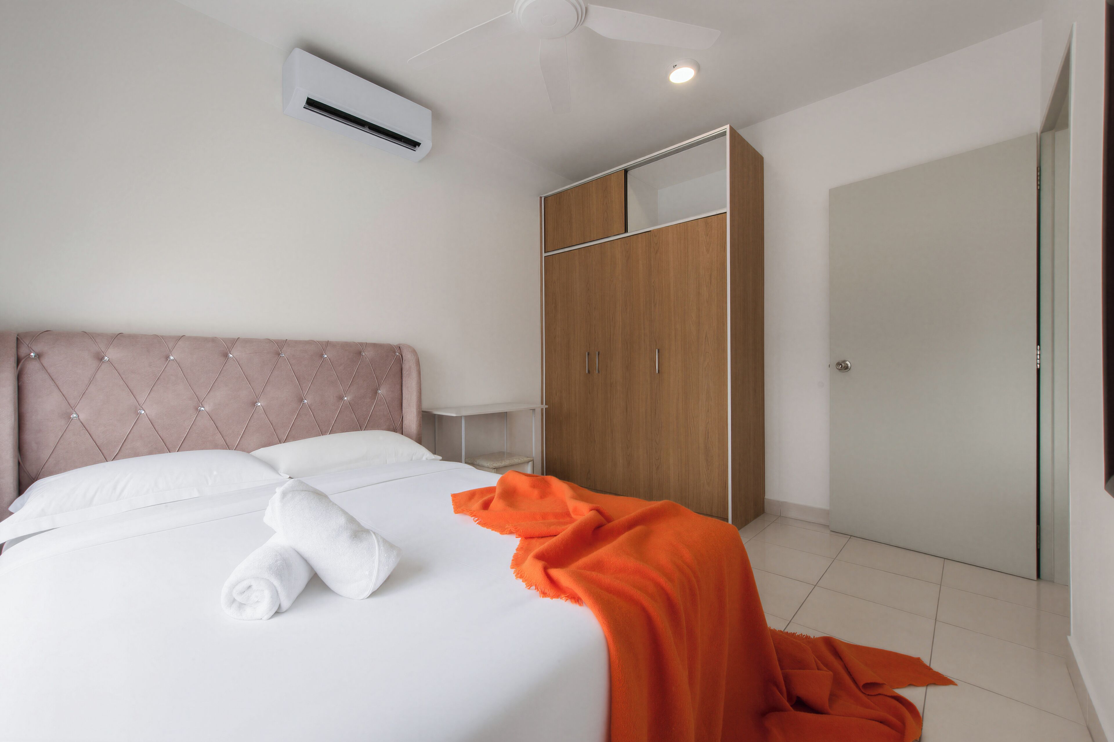 A hotel room with a bed, an air conditioner, a ceiling fan, a wardrobe, and a door.