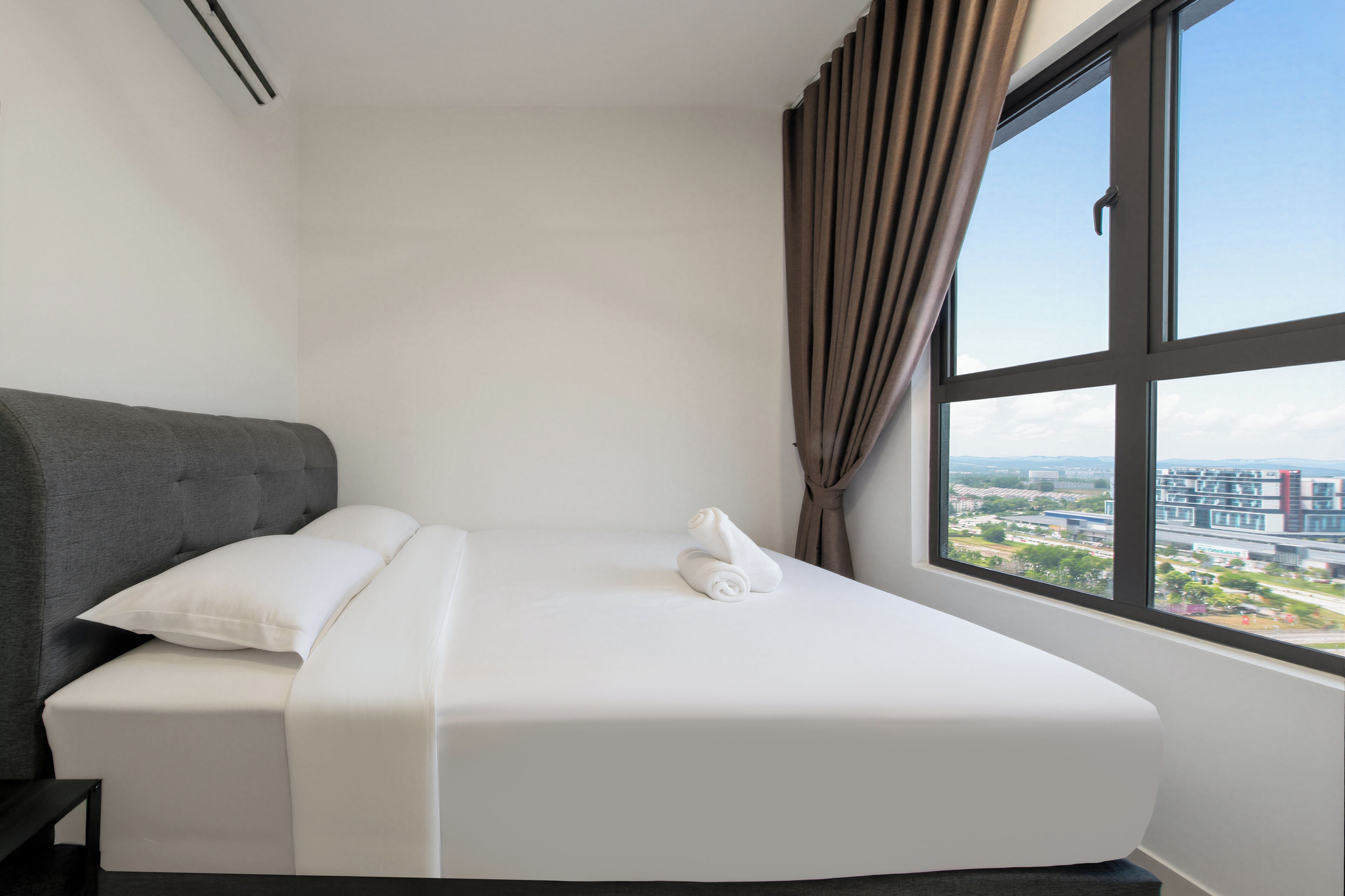 A modern hotel room with a large window, a bed with white linens, and a grey upholstered headboard.