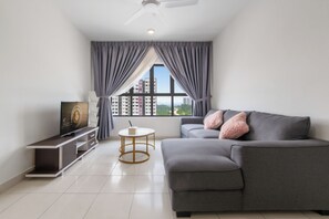 Een moderne woonkamer met een grijze bank, een flatscreen televisie, een klein rond tafeltje en een raam met gordijnen.