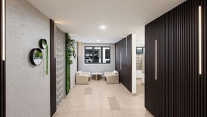Un corridoio dal design moderno, con un tavolo rotondo e due sedie, una parete divisoria in vetro con piante e una parete in legno scuro con luci a LED verticali.
