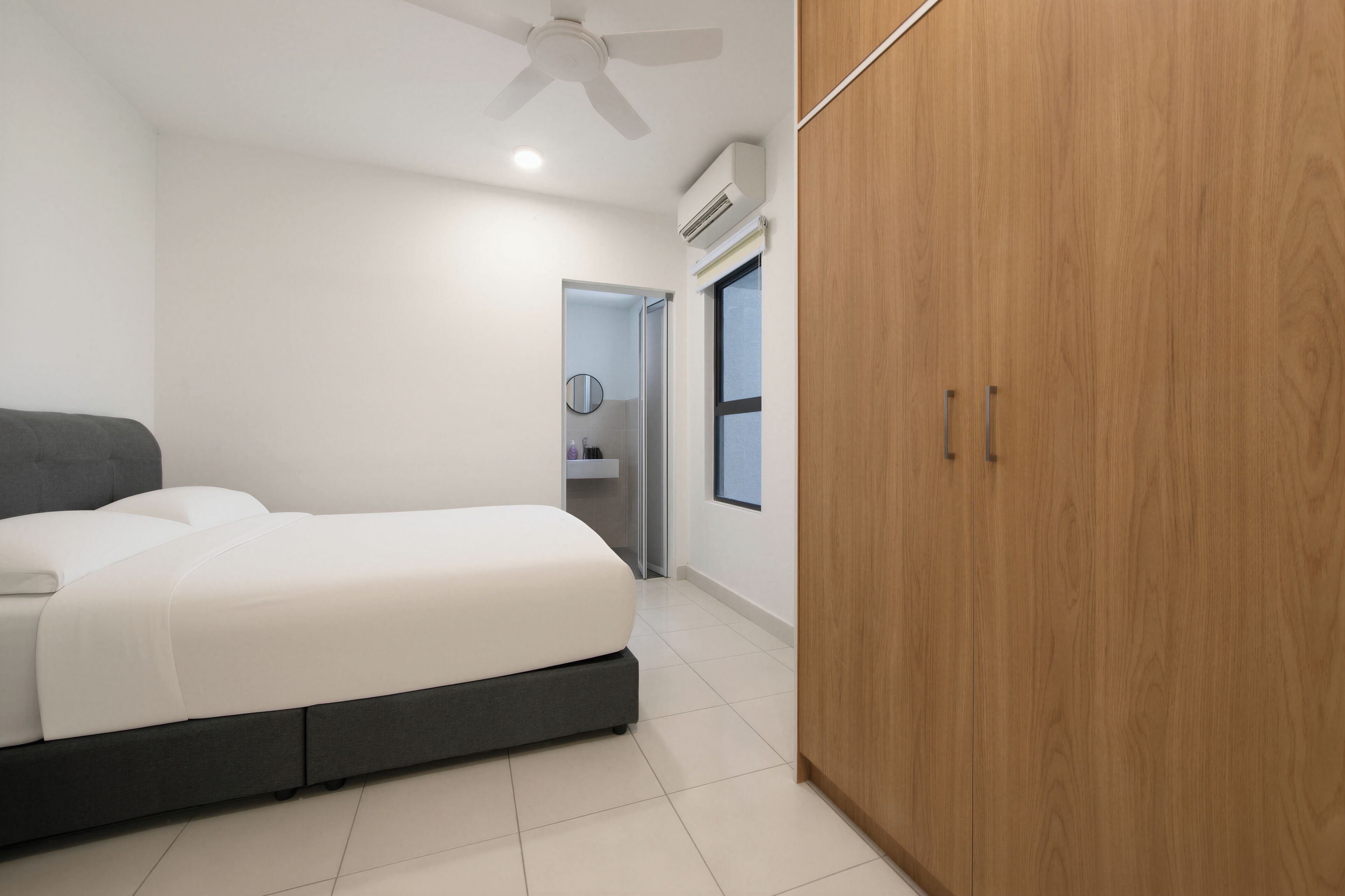 Une chambre à coucher moderne, équipée d’un lit, d’une armoire, d’un ventilateur de plafond, et dont la salle de bain est visible à travers une porte ouverte.
