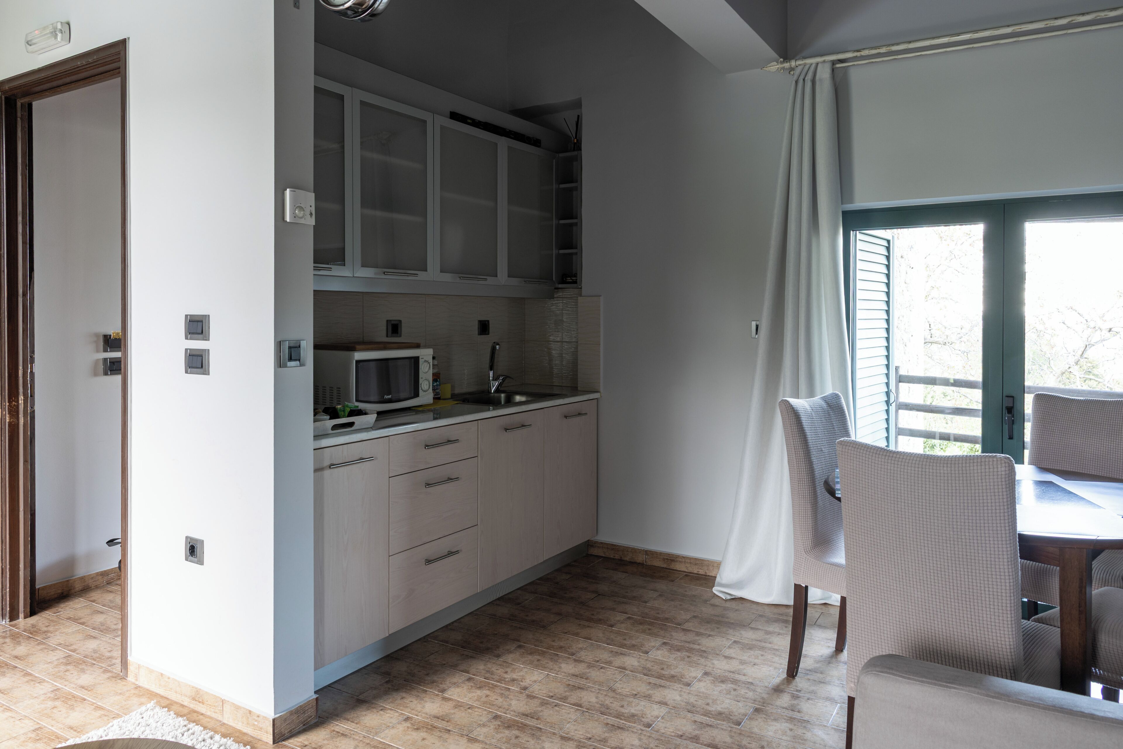 Een kleine keuken met witte kastjes, een magnetron en een eethoek met stoelen.
