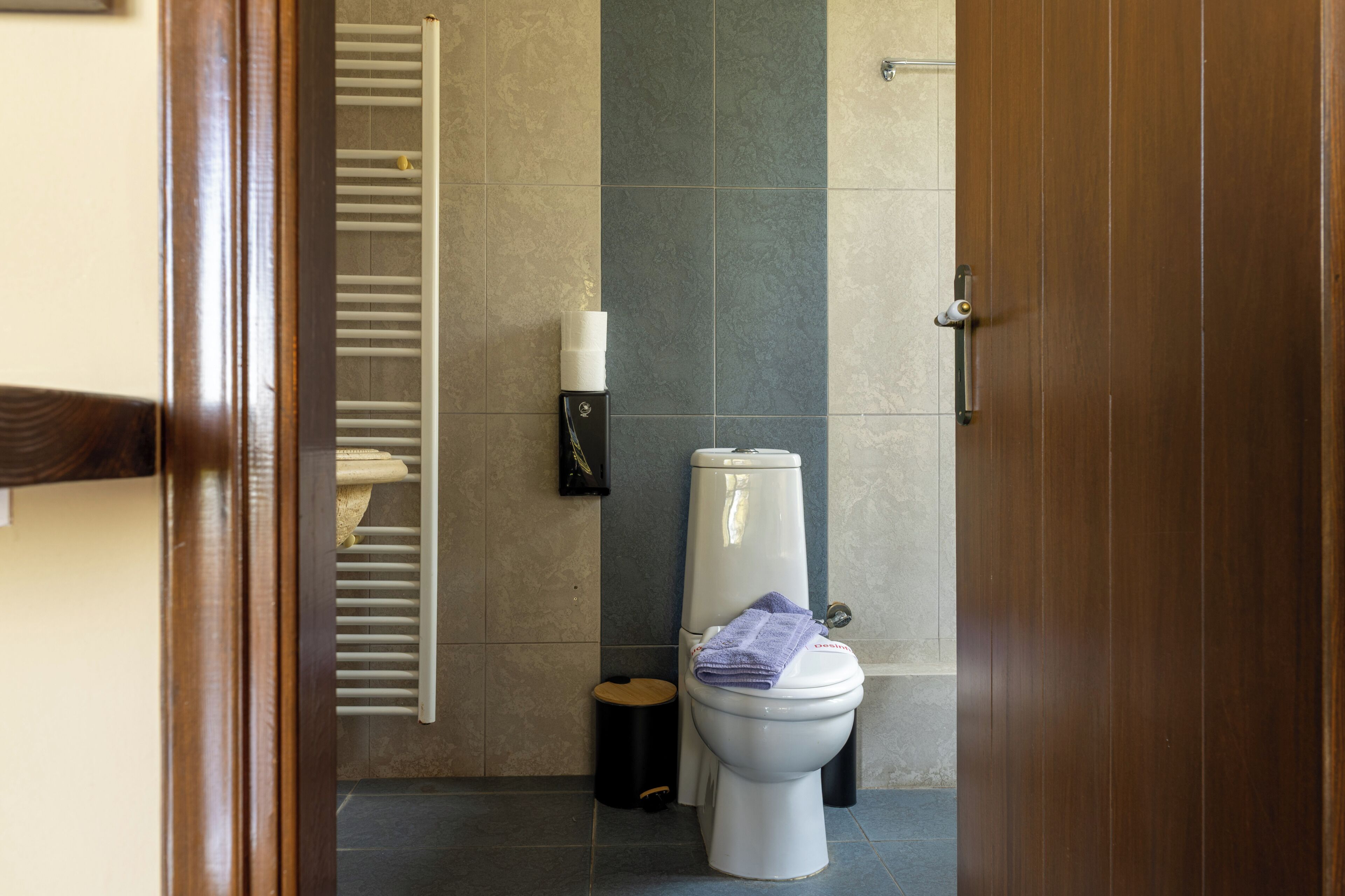 Un baño pequeño con inodoro, dispensador de toallas y cubo de basura.