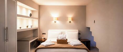 A hotel room with a bed, a wardrobe, a shelf with toiletries, two wall-mounted lights, and a nightstand with a lamp.
