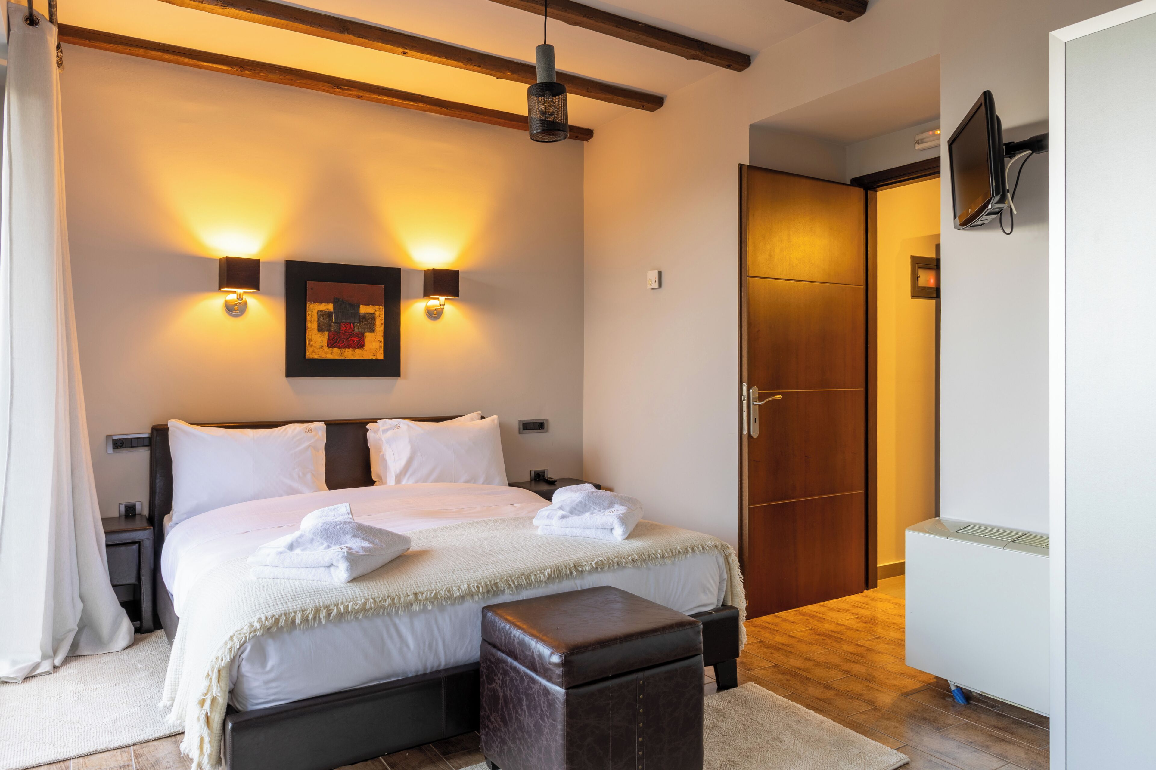 Un dormitorio con cama, mesitas de noche, televisor montado en la pared, una puerta de madera y un radiador.