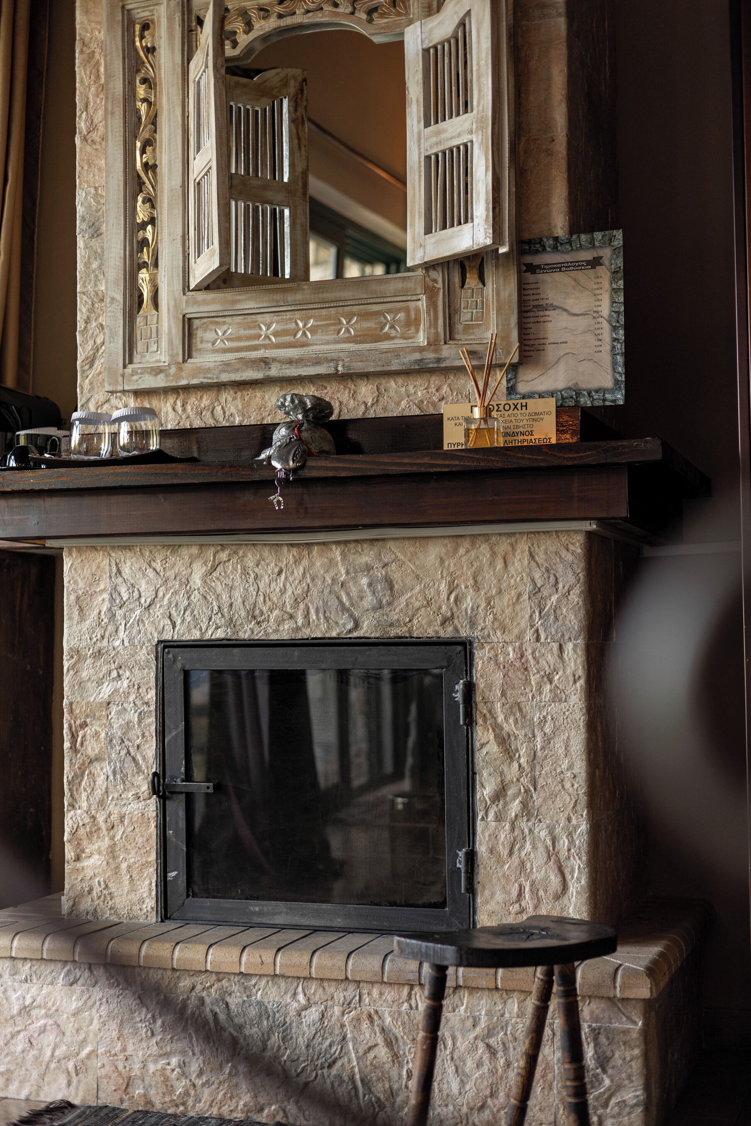 A stone fireplace with a black glass door, a decorative mirror above it, and a small shelf with items.
