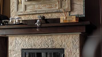 A stone fireplace with a black glass door, a decorative mirror above it, and a small shelf with items.
