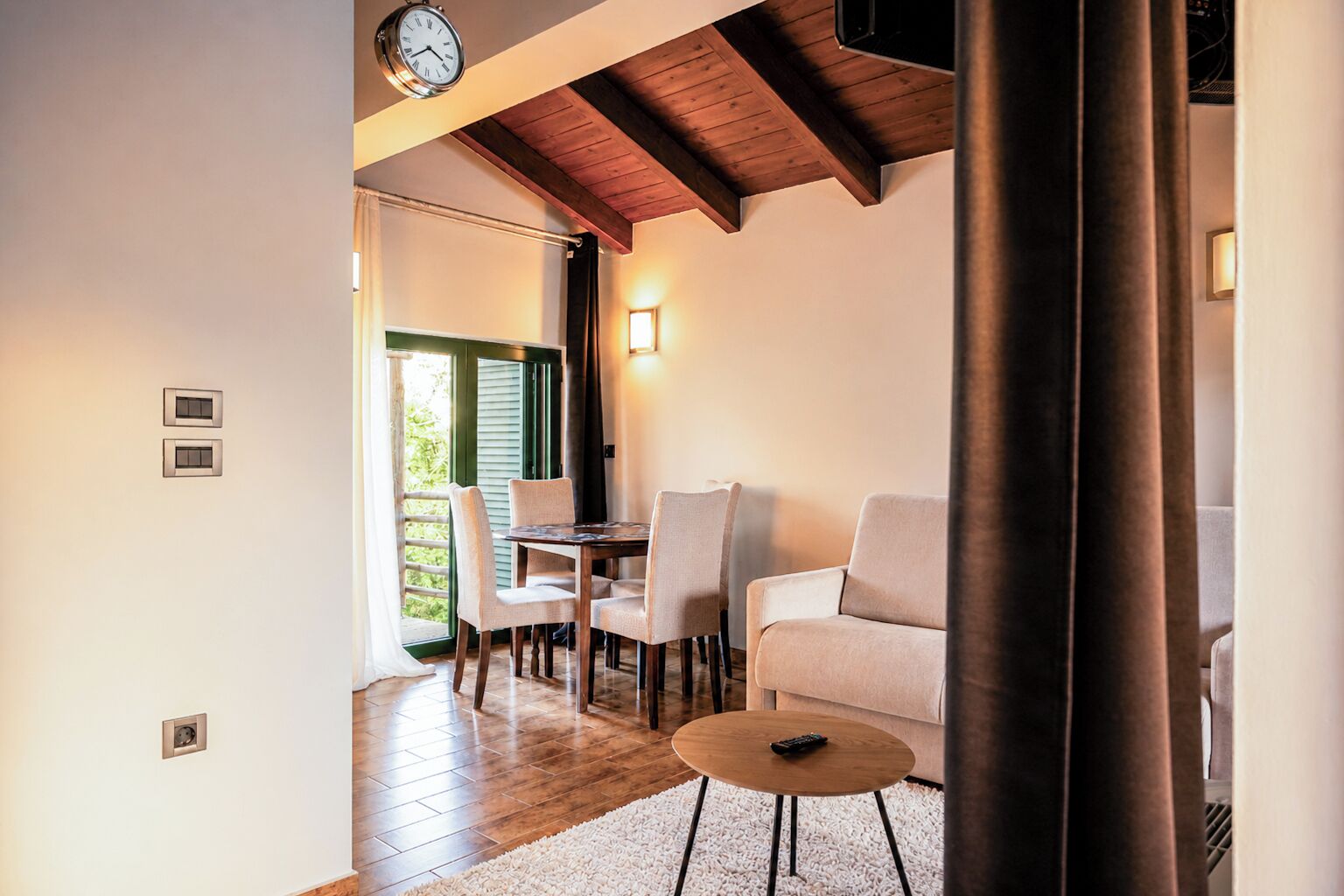 Una habitación con techo de madera, una mesa de comedor con sillas, un sofá y una pequeña mesa redonda con un control remoto.