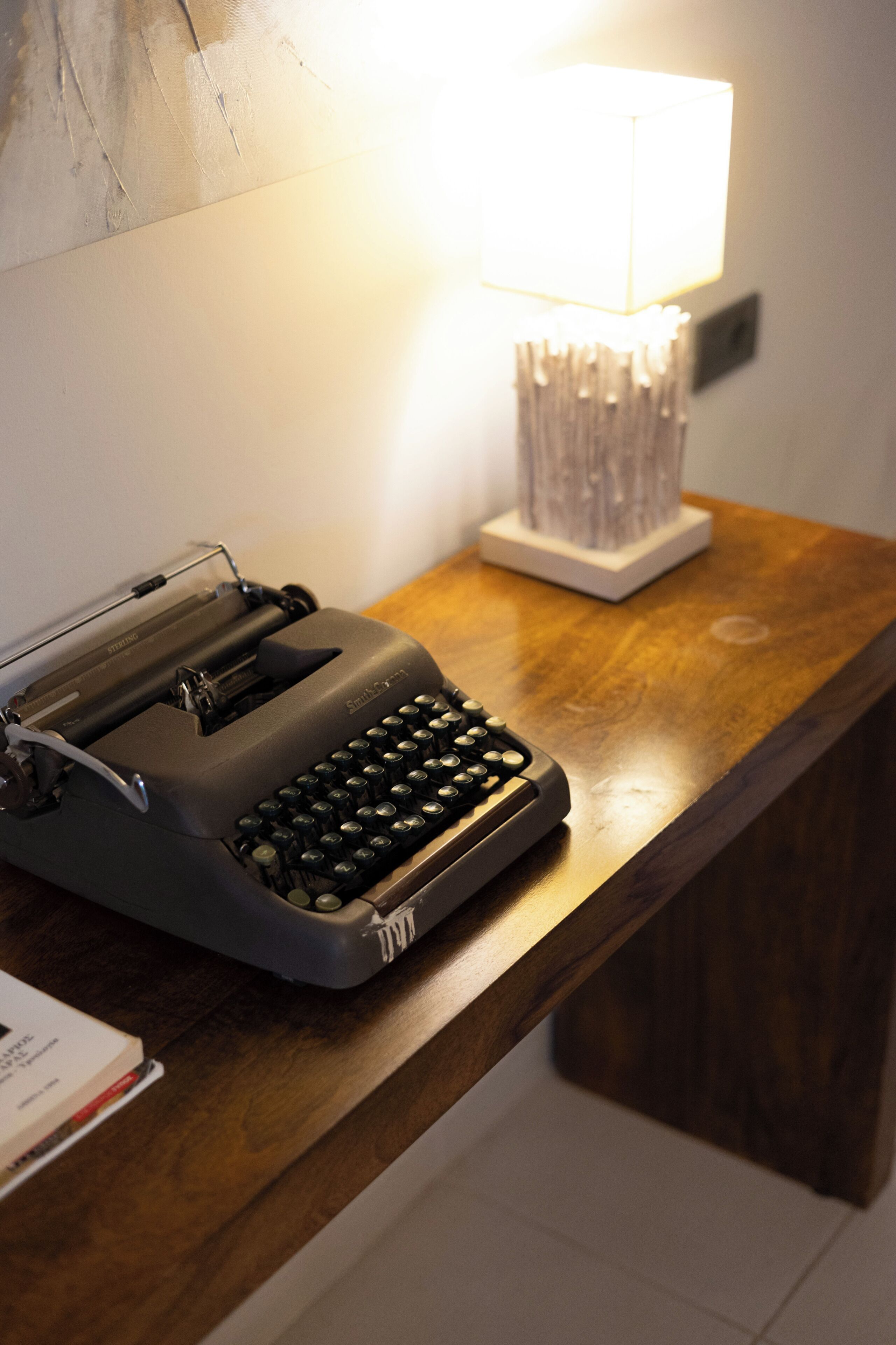 A typewriter on a wooden desk with a lamp in the background.