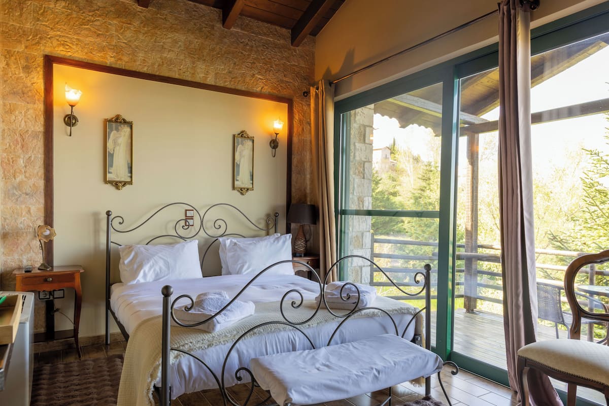 Ein Schlafzimmer mit Bett, Nachttisch, Lampe und Blick ins Freie.