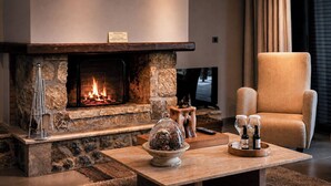 A stone fireplace with a lit fire, a comfortable armchair, a coffee table with decorative items, and a television mounted on the wall. - Vathyskia Guesthouse (Xylokastro-Evrostina)