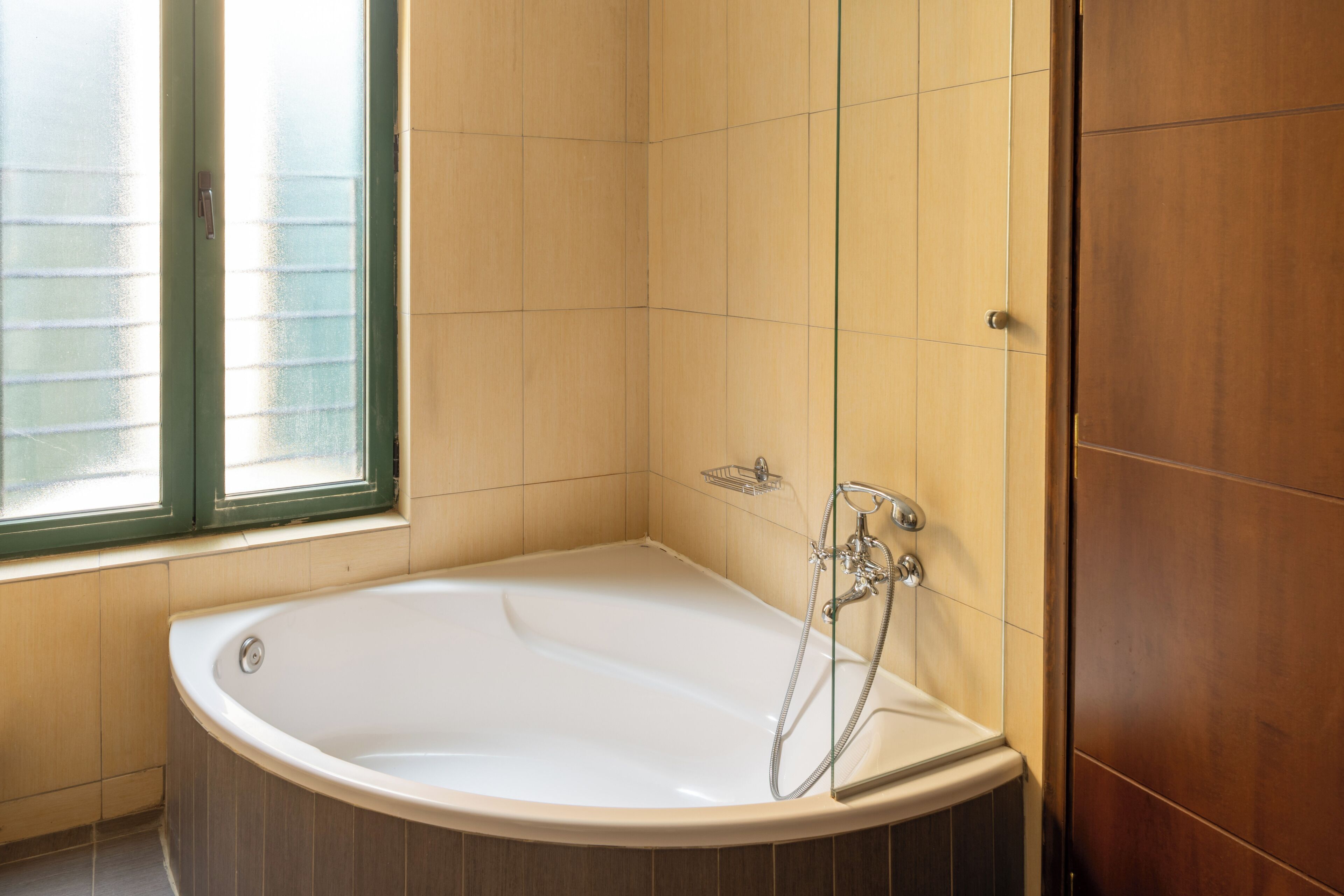 A bathroom with a bathtub, a window, and wooden walls.