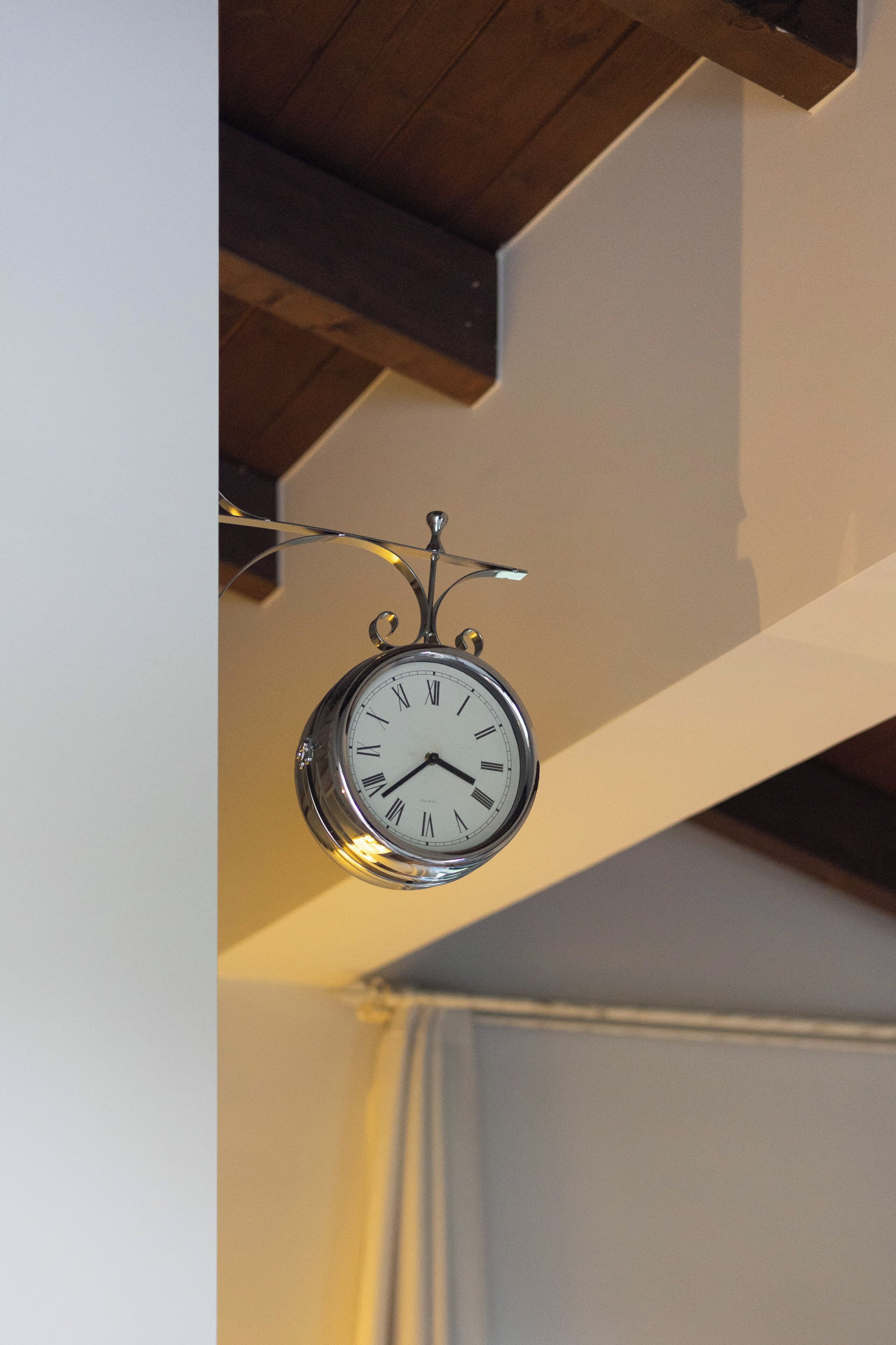 Eine an der Wand befestigte Wanduhr mit römischen Ziffern und Pendel, die an einer Decke mit freiliegenden Holzbalken hängt.