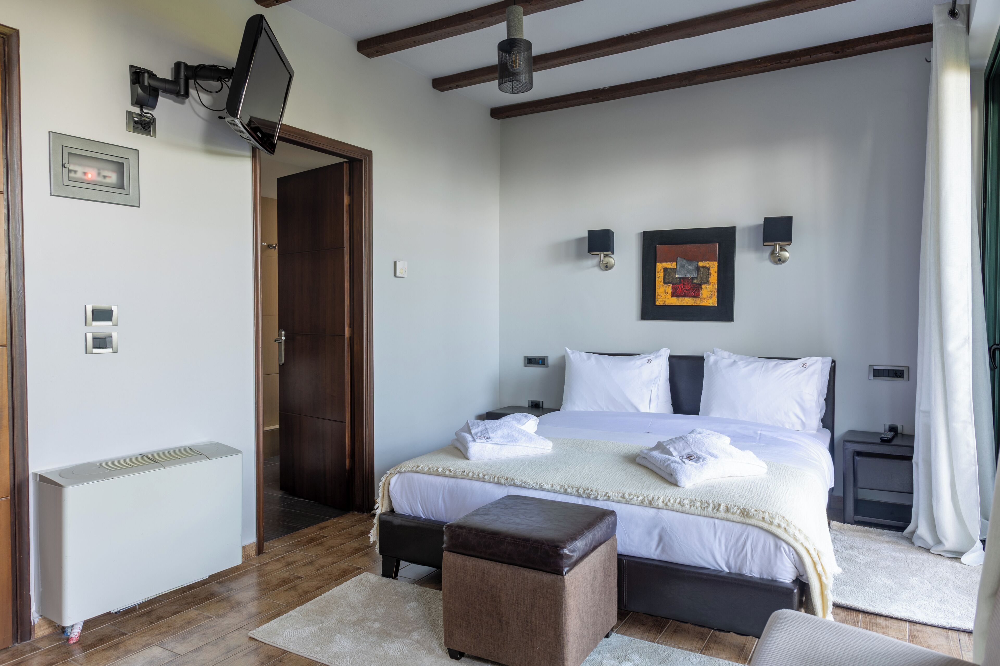 A bedroom with a bed, bedside tables, a TV mounted on the wall, and a heater.
