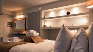 A hotel room with a bed, a bedside table, a mirror, a shelf with toiletries, and a wall-mounted clock. - Vathyskia Guesthouse (Xylokastro-Evrostina)