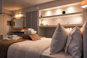 A hotel room with a bed, a bedside table, a mirror, a shelf with toiletries, and a wall-mounted clock. - Vathyskia Guesthouse (Xylokastro-Evrostina)