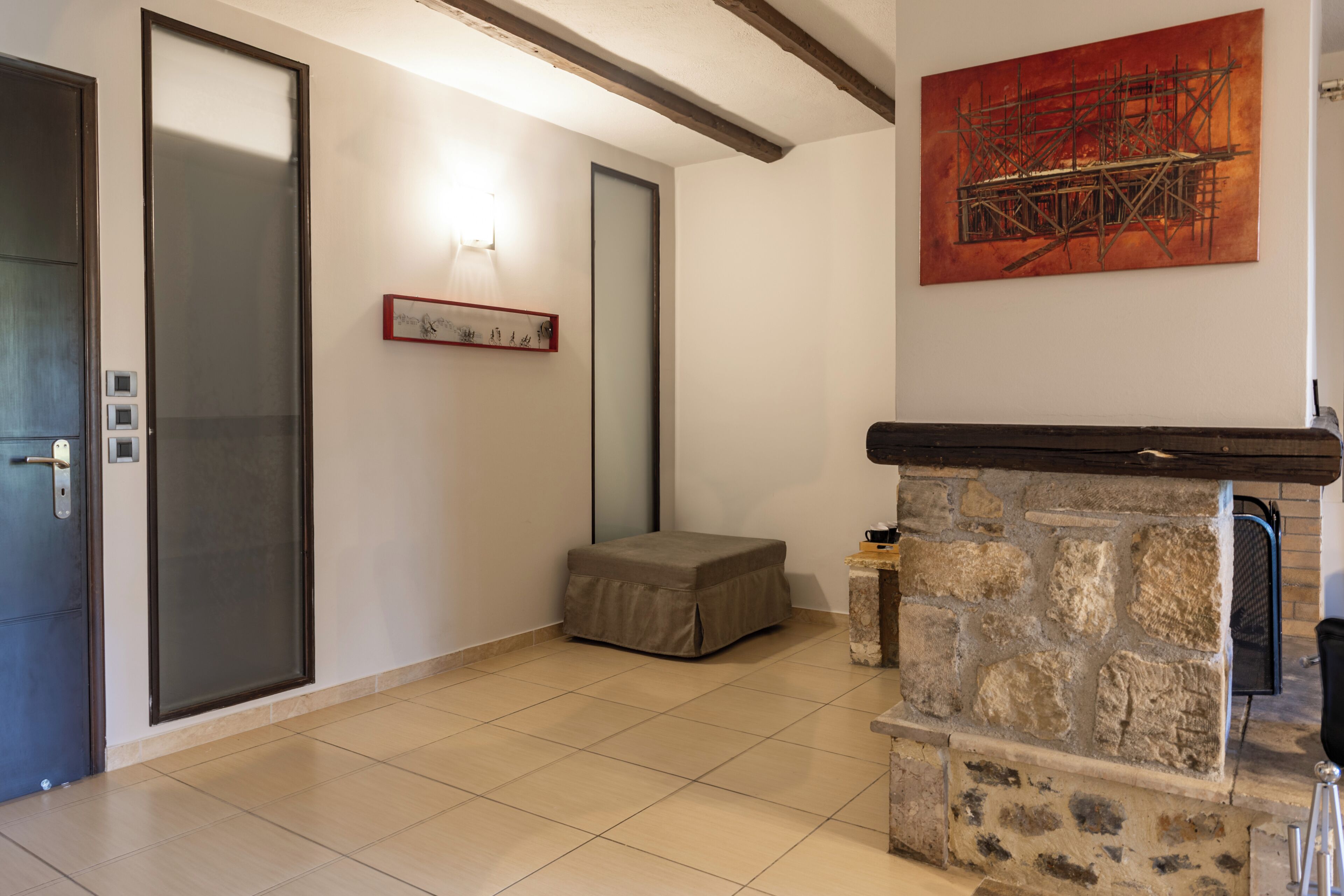 A room with a stone fireplace, a framed artwork, a bench, and a door with frosted glass panels.