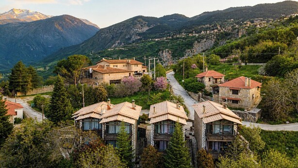 A hillside village with stone houses, a winding road, and mountains in the background. - Vathyskia Guesthouse (Xylokastro-Evrostina)