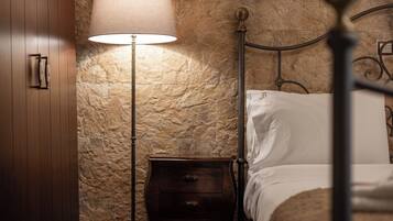 Un dormitorio con pared de piedra, mesita de noche de madera con lámpara y estructura de cama metálica.