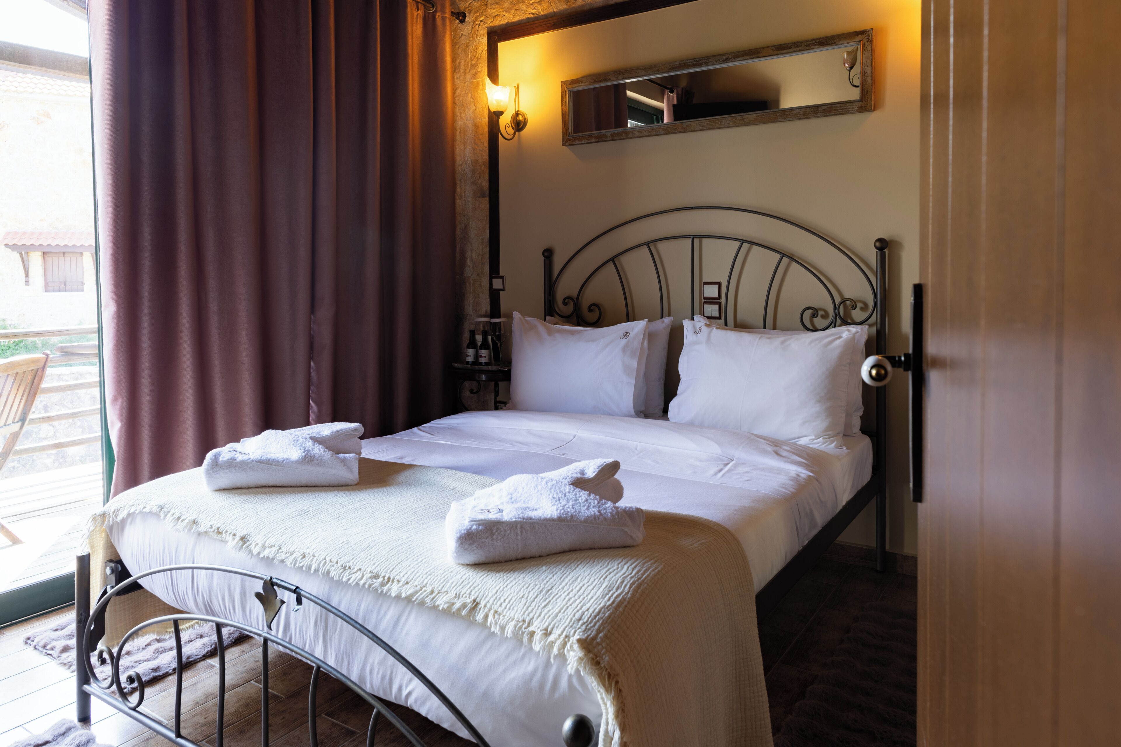 Una cama bien tendida con almohadas y una manta, una mesita de noche con lámpara, y una ventana con cortinas.