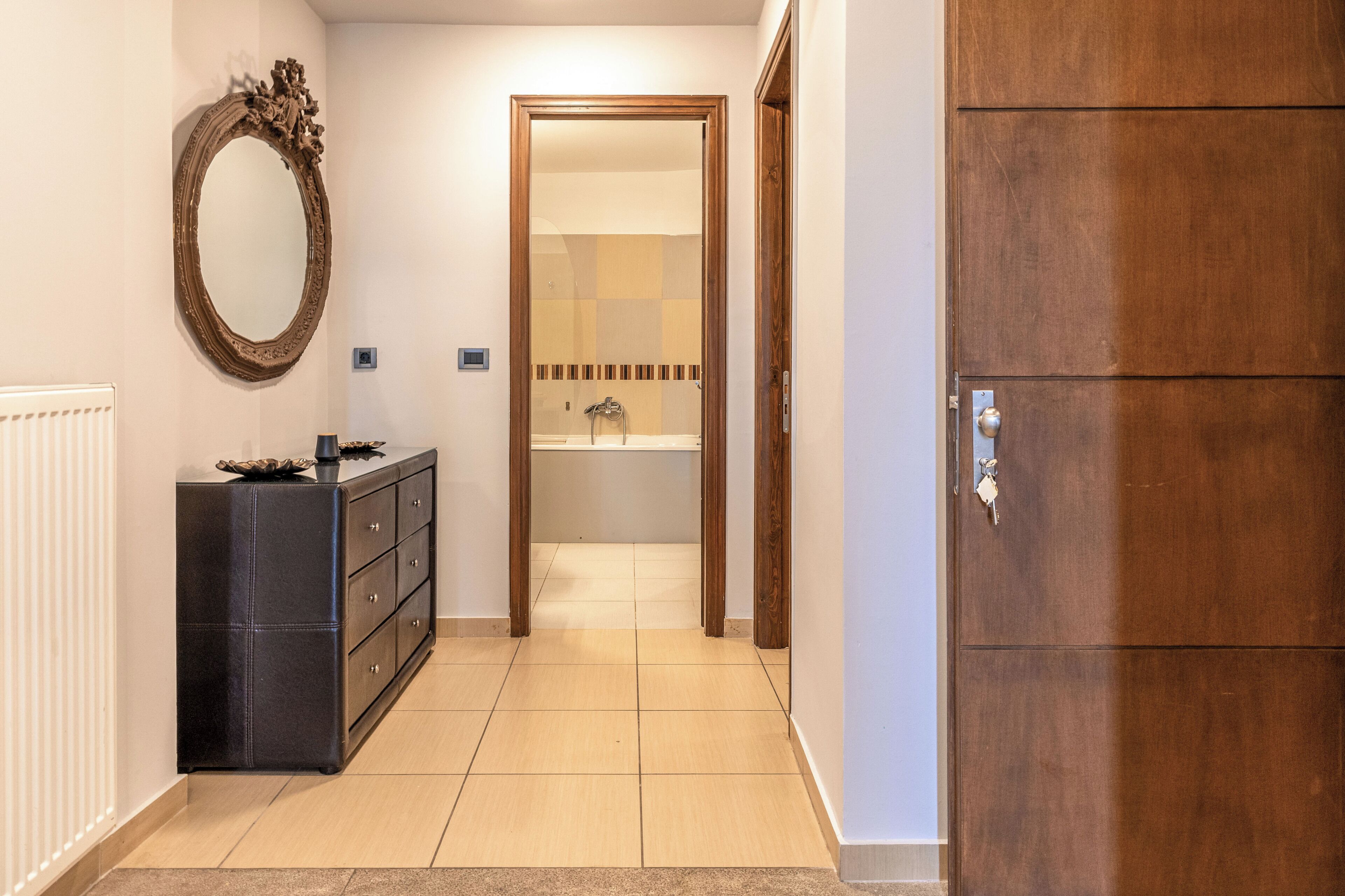A hallway with a black dresser, a wooden door, and a mirror on the wall.