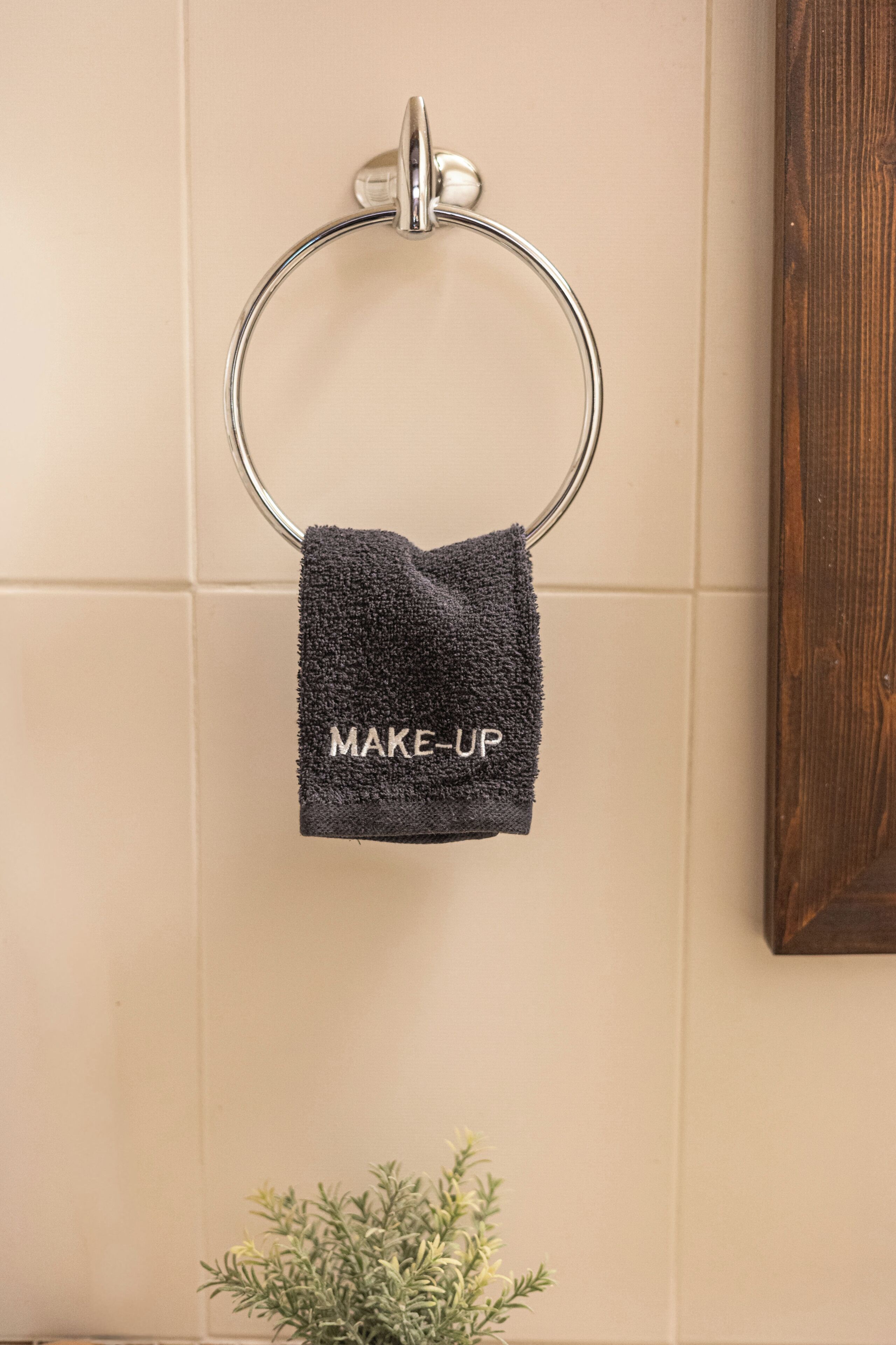 A bathroom with a towel ring, a towel with 'MAKE-UP' text, and a potted plant.