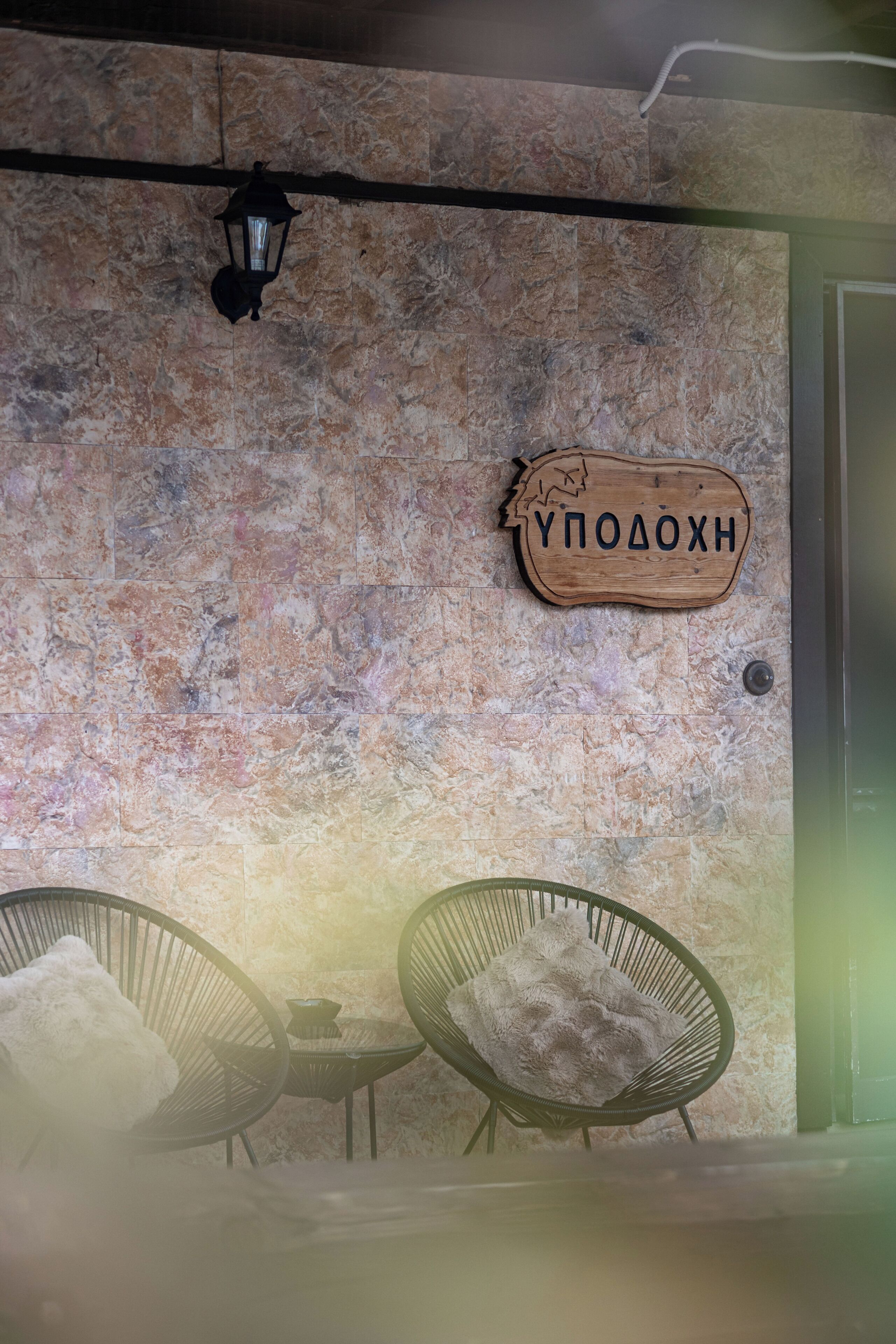 A stone wall with a wooden sign reading 'УПОЛОЖН' and two wicker chairs with fluffy cushions.