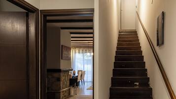 Una escalera de madera con barandilla que conduce a un área de comedor con chimenea de piedra y sillas.