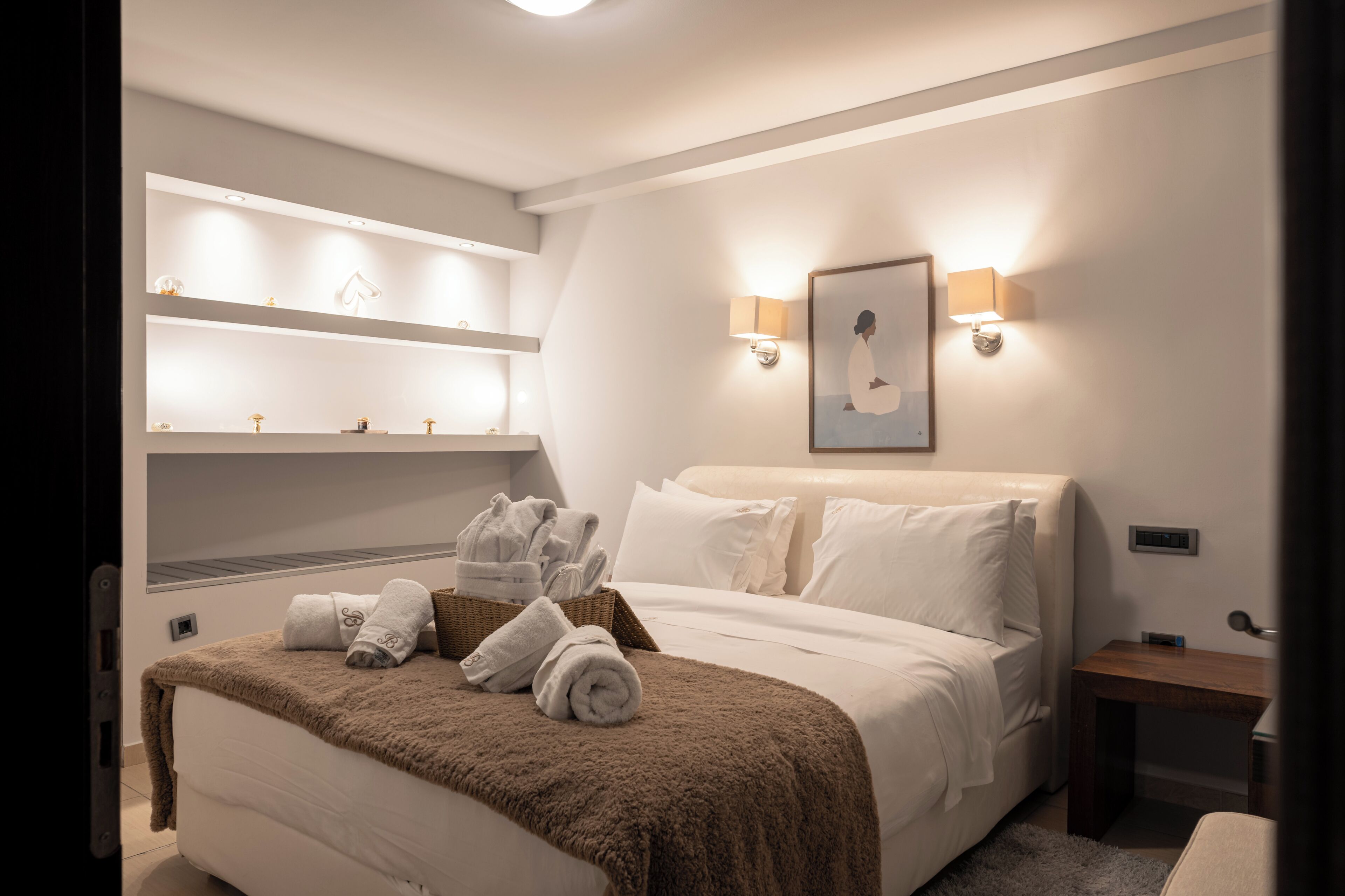 Een hotelkamer met een bed, een wandplank met toiletartikelen, een nachtkastje en een wandlamp.