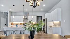Una cocina moderna con una mesa de comedor de madera, taburetes de bar, lámparas colgantes y una isla central con una planta en maceta.