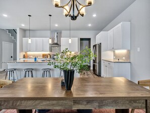 Eine moderne Küche mit Holztisch, Barhocker, Pendelleuchten und einer zentralen Kochinsel mit Blumentopf.