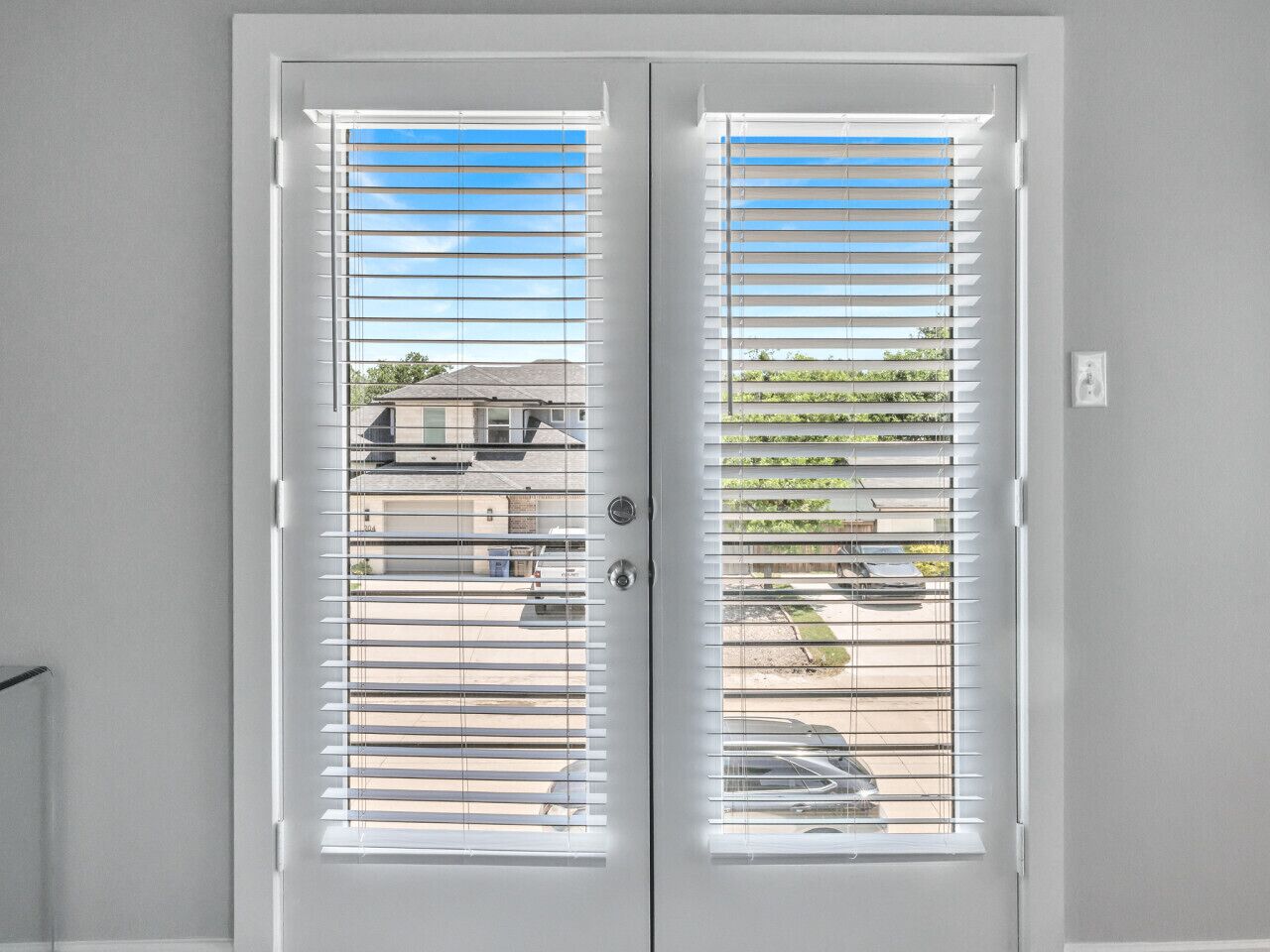 A double door with horizontal blinds, a visible lock, and a small light switch on the wall.