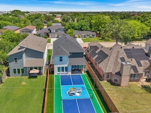 A residential area with houses, a tennis court, and a large blue logo on the court.