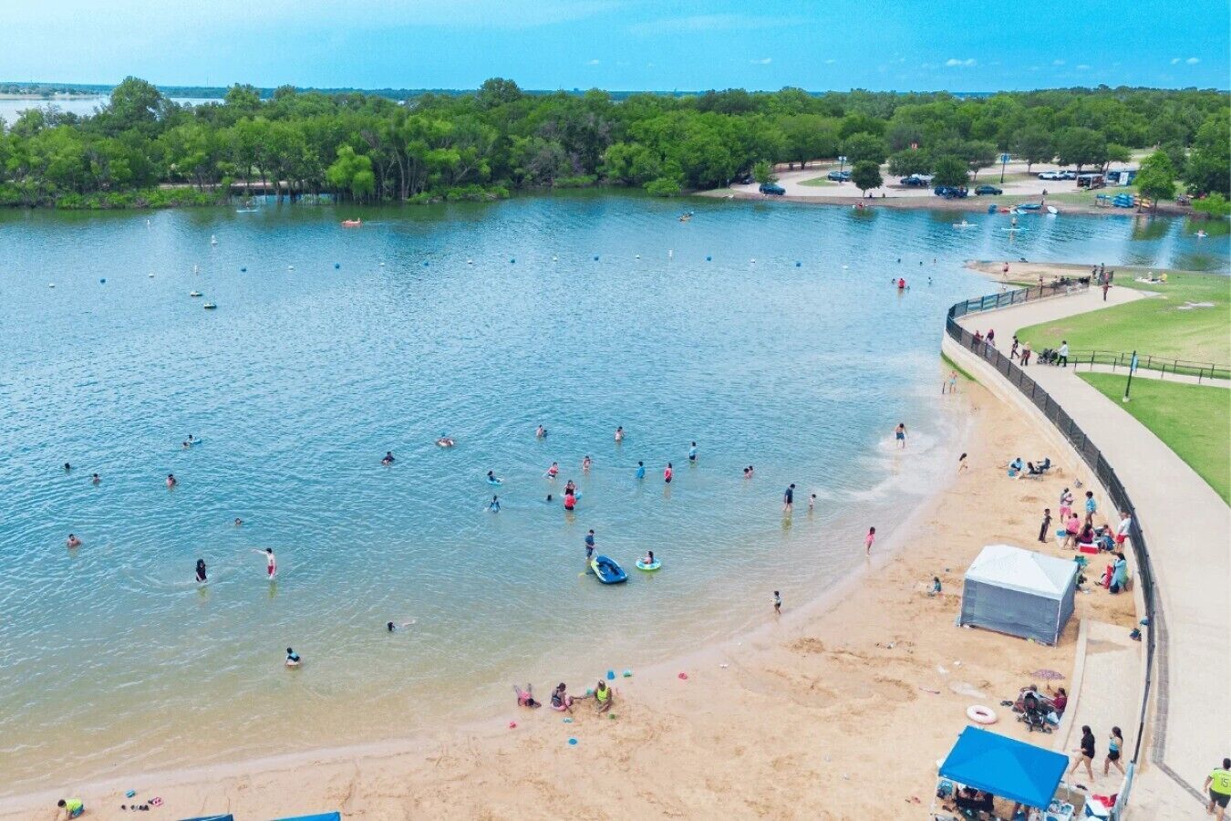 A lakeside beach with people swimming and walking along the shore.