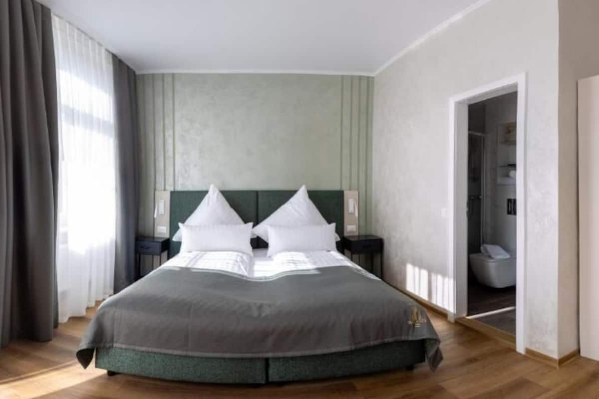 A large bed with a green headboard, two bedside tables, and a view into a bathroom.