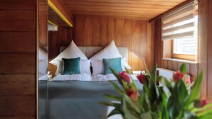 Ein Zimmer mit Holzwänden, einem Bett, Kissen, einem Nachttisch und einem Fenster mit Jalousien.