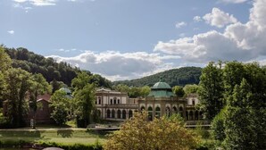 Ein historisches Gebäude mit einer grünen Kuppel, umgeben von üppigem Grün und blauem Himmel.