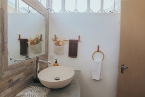 A bathroom with a large round sink, a mirror, and a towel rack with multiple towels. - Cozy 2-bedroom apartment in charming Tamarin with AC (Tamarin)