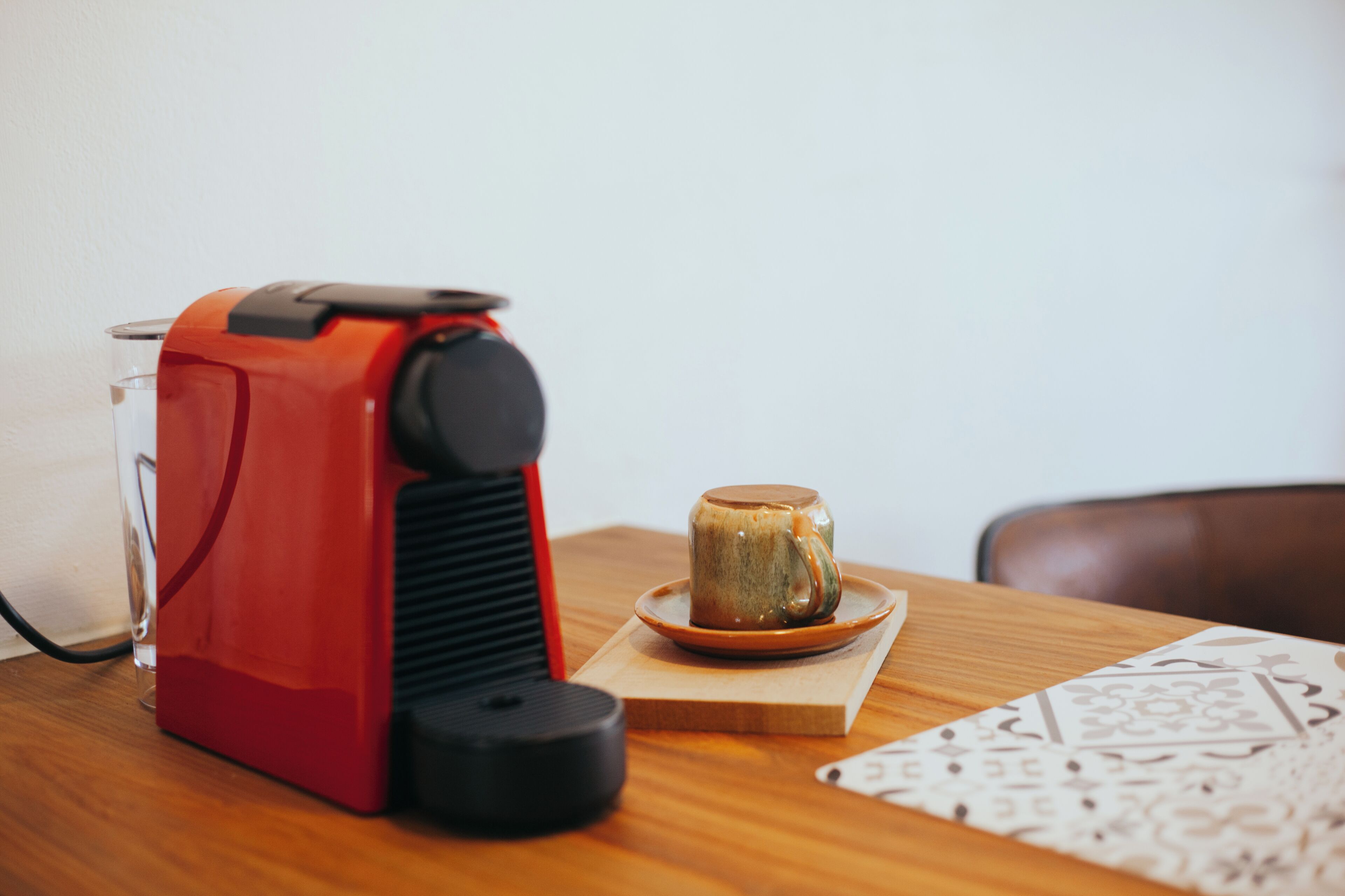 A red coffee machine, a glass, and a ceramic mug on a wooden table.