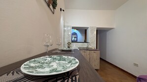 Uma área de refeições com uma mesa posta para dois, cozinha ao fundo e um espelho sobre a pia.
