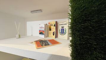 Een receptiebalie met een witte toonbank, een kleine plant en drie boeken met de titels 'Sabina', 'Configui' en 'Pro-Loco di Confinio'.