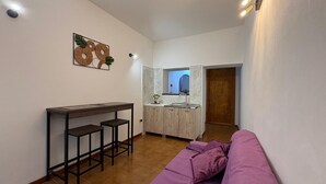Um espaço compacto com cozinha compacta, área de refeições com banquetas e um sofá roxo.