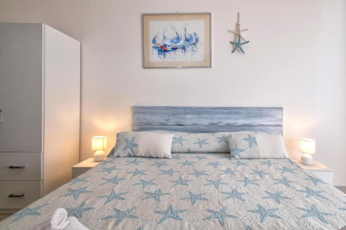 A bedroom with a bed, nightstands, a wardrobe, a framed artwork, and a starfish decoration.