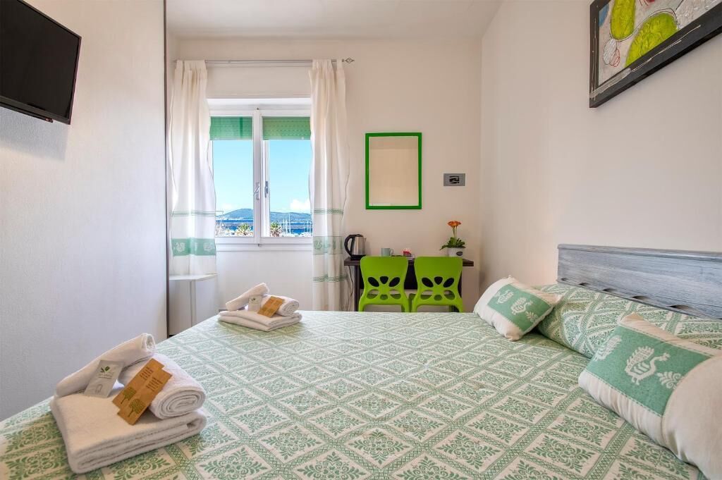 A hotel room with a bed, a desk, a chair, and a view of the sea.