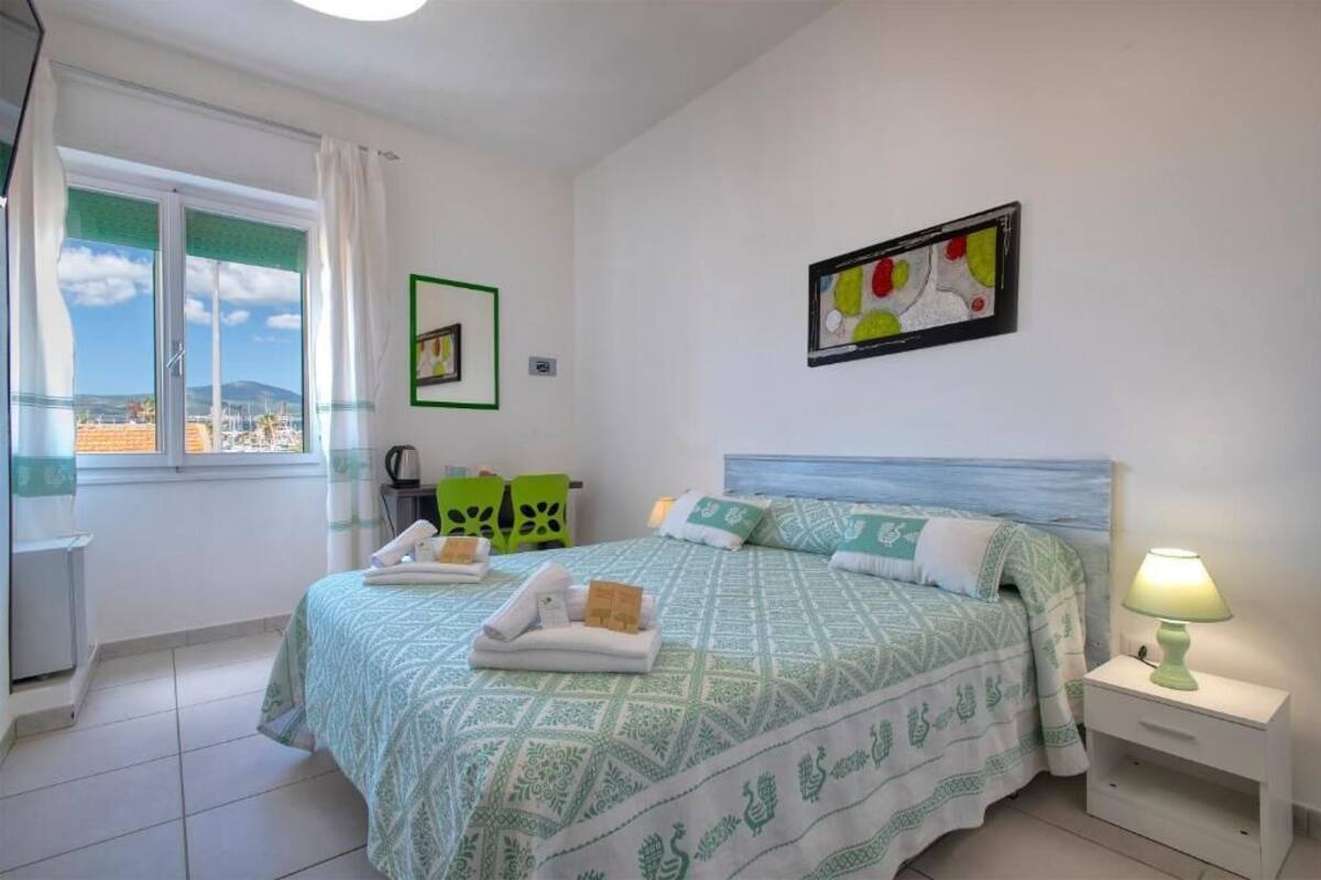 A hotel room with a bed, a nightstand, a chair, a window with curtains, and a painting on the wall.