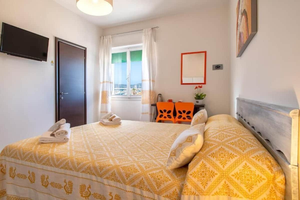 A hotel room with a bed, a desk, a chair, a TV, and a window with curtains.