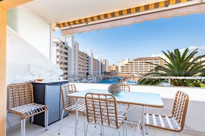 Een balkon met een tafel en stoelen, een kitchenette en uitzicht op een zwembad en gebouwen.